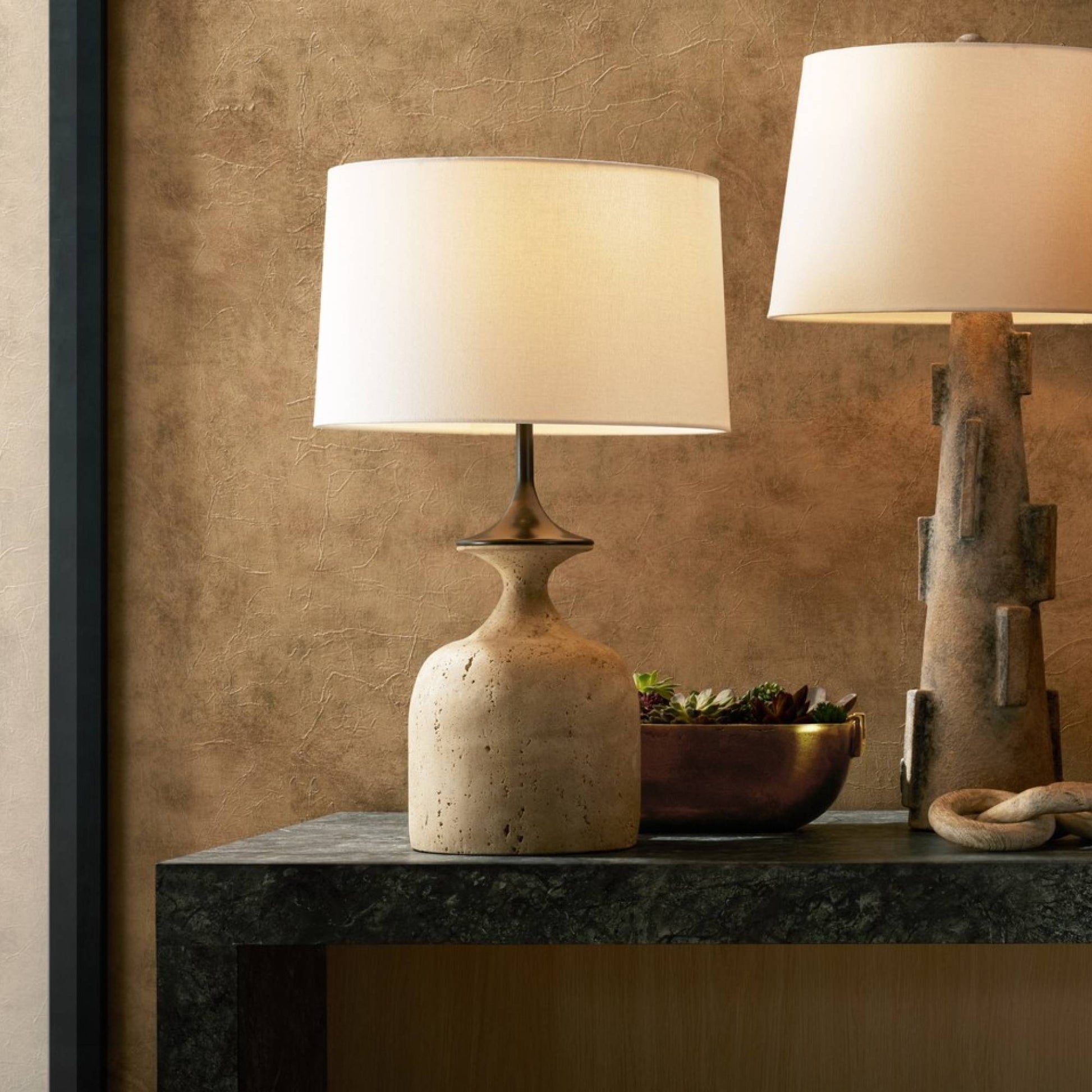Two table lamps on a dark surface with a textured wall background