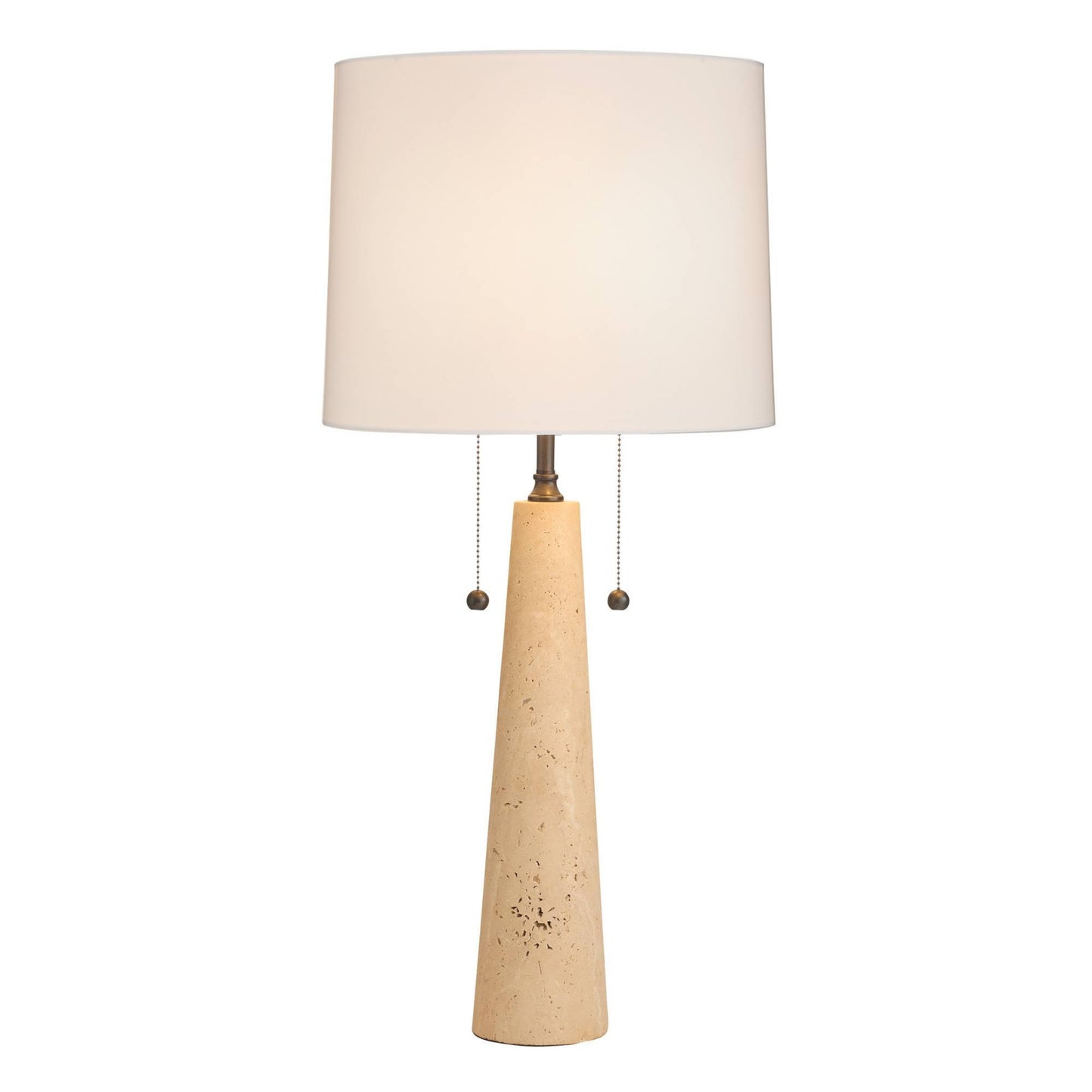 A table lamp with a tapered beige stone base, a white fabric drum shade, and a brass pull chain with small round beads.