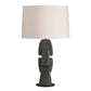 A table lamp with a textured, stacked ceramic base in a dark gray-green glaze and a large, plain off-white fabric drum shade, shown against a solid white background.