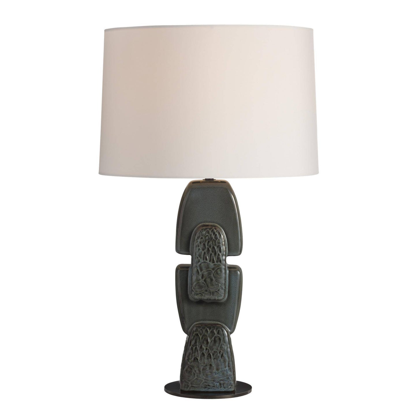 A table lamp with a textured, stacked ceramic base in a dark gray-green glaze and a large, plain off-white fabric drum shade, shown against a solid white background.