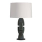A table lamp with a large white drum shade and a sculptural ceramic base in a dark charcoal gray with subtle blue-green glaze accents, set against a plain white background.