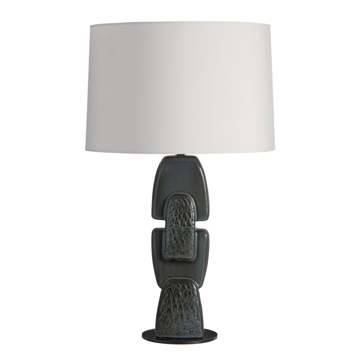 A table lamp with a large white drum shade and a sculptural ceramic base in a dark charcoal gray with subtle blue-green glaze accents, set against a plain white background.