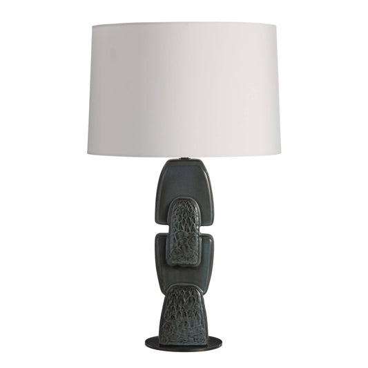 A table lamp with a large white drum shade and a sculptural ceramic base in a dark charcoal gray with subtle blue-green glaze accents, set against a plain white background.