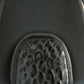 A close-up of a textured gray surface with a rounded, glossy, honeycomb-like metallic or glass insert at the bottom.
