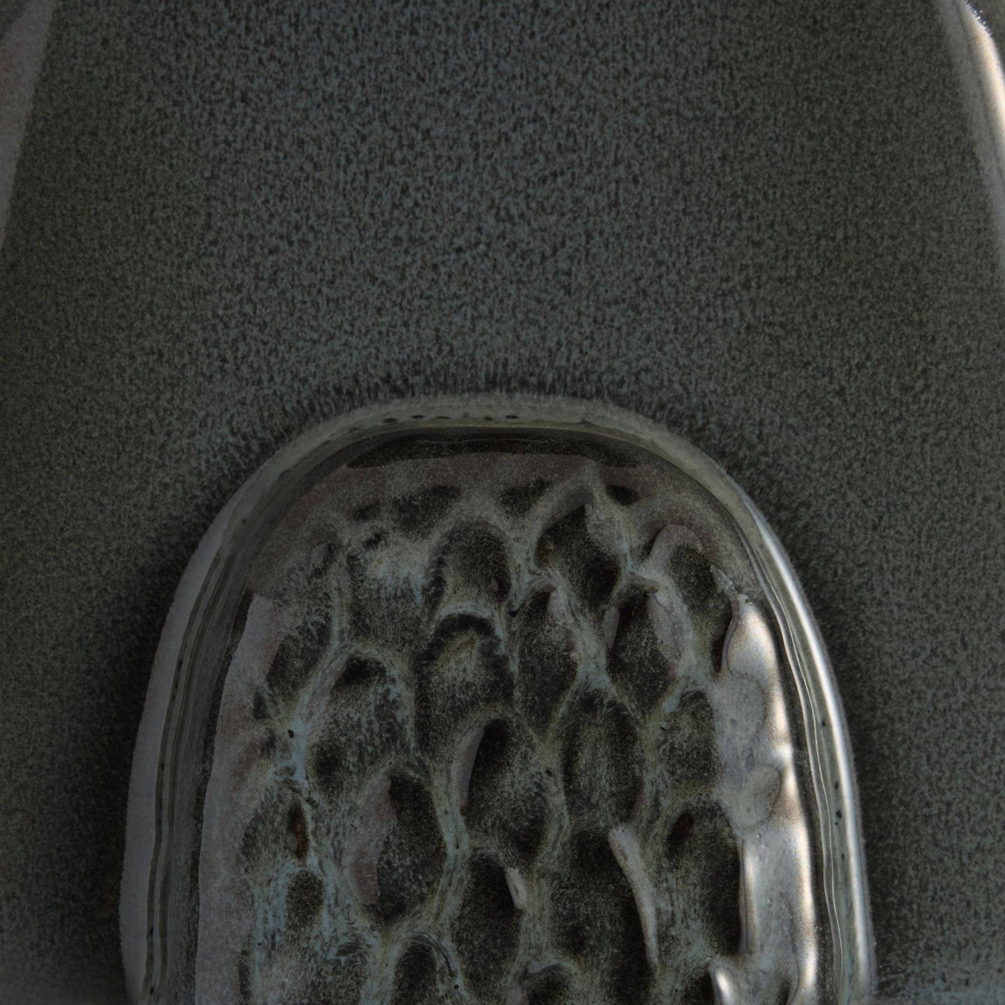 A close-up of a textured gray surface with a rounded, glossy, honeycomb-like metallic or glass insert at the bottom.