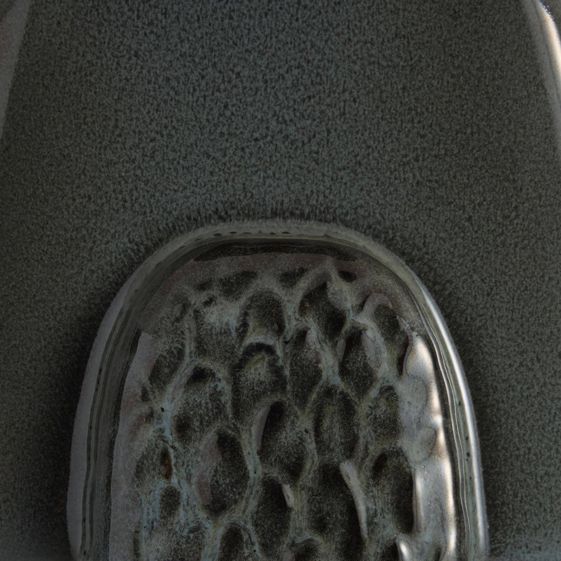 A close-up of a textured gray surface with a rounded, glossy, honeycomb-like metallic or glass insert at the bottom.