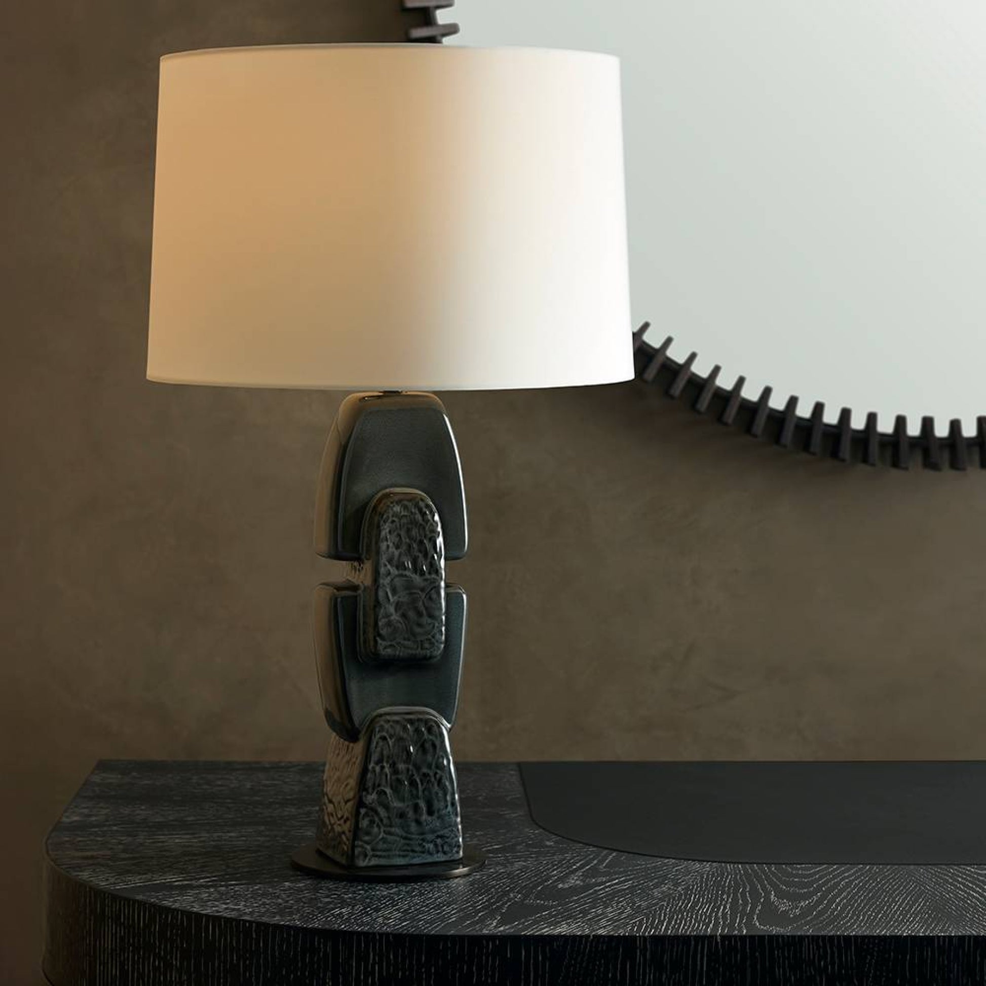 Table lamp with textured base and white shade on a dark surface against a brown wall.