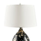 Decorative table lamp with a black base featuring gold speckles and a white shade on a white background.