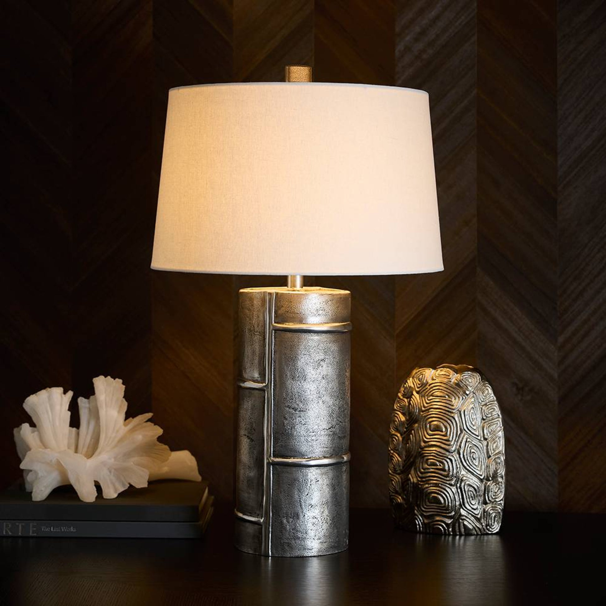 Table lamp with textured metal base and white shade on a dark surface with decorative items.