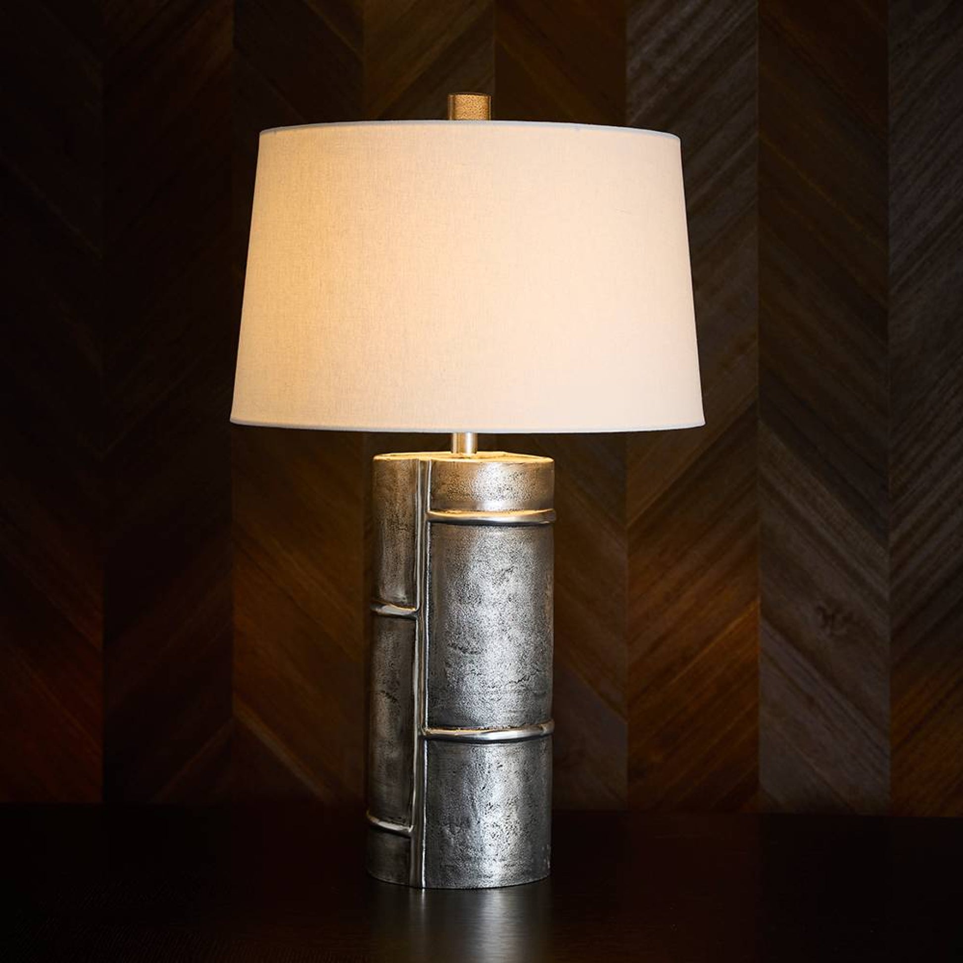 Table lamp with metallic base and beige shade against a wooden paneled wall.