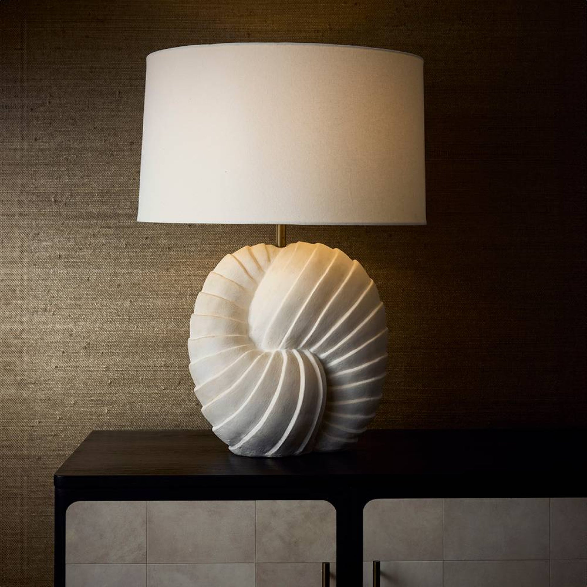 Decorative lamp with shell design on a dark surface against a textured wall.