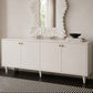 A white mid-century modern sideboard cabinet with four doors and small brass knobs, styled with a matching white textured sunburst mirror on top and a black bowl on books. The cabinet stands on dark wood flooring over a black and white striped rug against a neutral beige wall.
