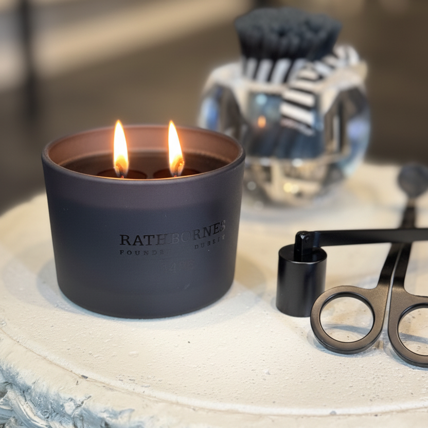 Lit candle in a black container with 'Ratner & Rose' branding on a textured surface.