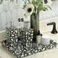 Bathroom counter with black and white mosaic tray, decorative bottles, and a vase with flowers.
