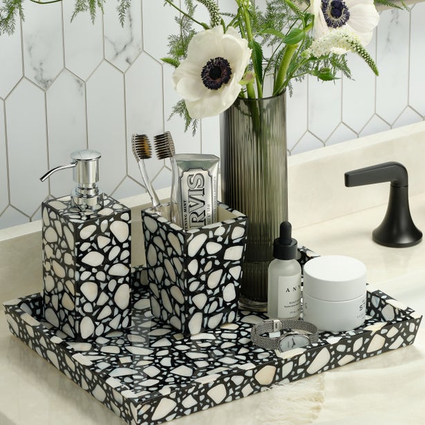 Bathroom counter with black and white mosaic tray, decorative bottles, and a vase with flowers.