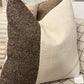 Two textured pillows, one brown and one beige, on a sofa with a visible tag.