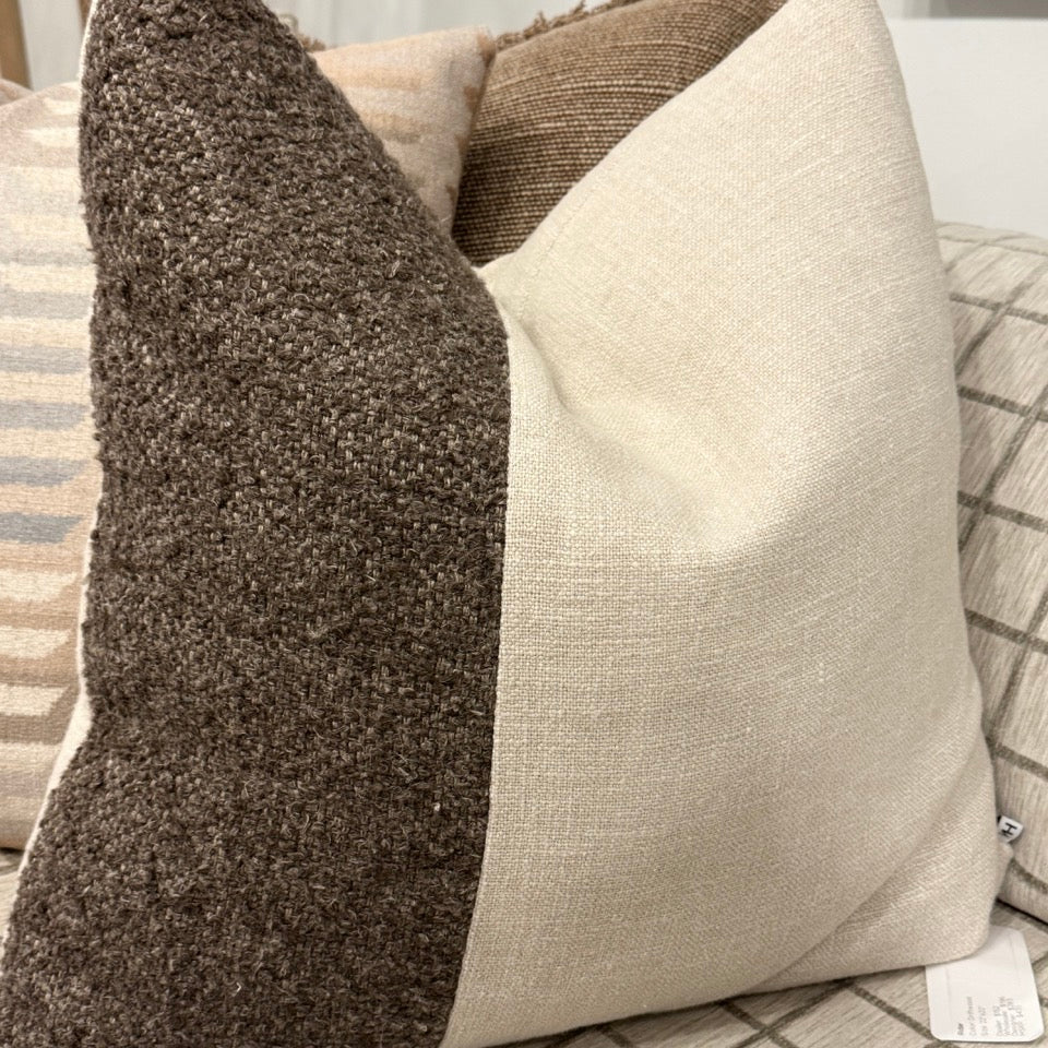 Two textured pillows, one brown and one beige, on a sofa with a visible tag.