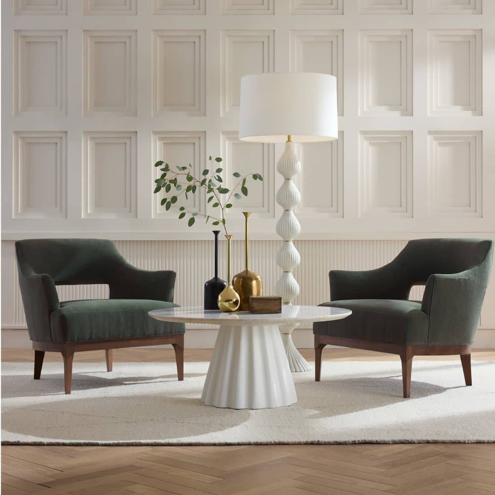 Modern living room with two green chairs and a white table against a paneled wall.