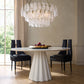 Dining room with a modern chandelier, white table, and black chairs.