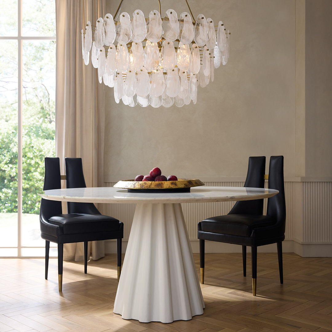 Dining room with a modern chandelier, white table, and black chairs.