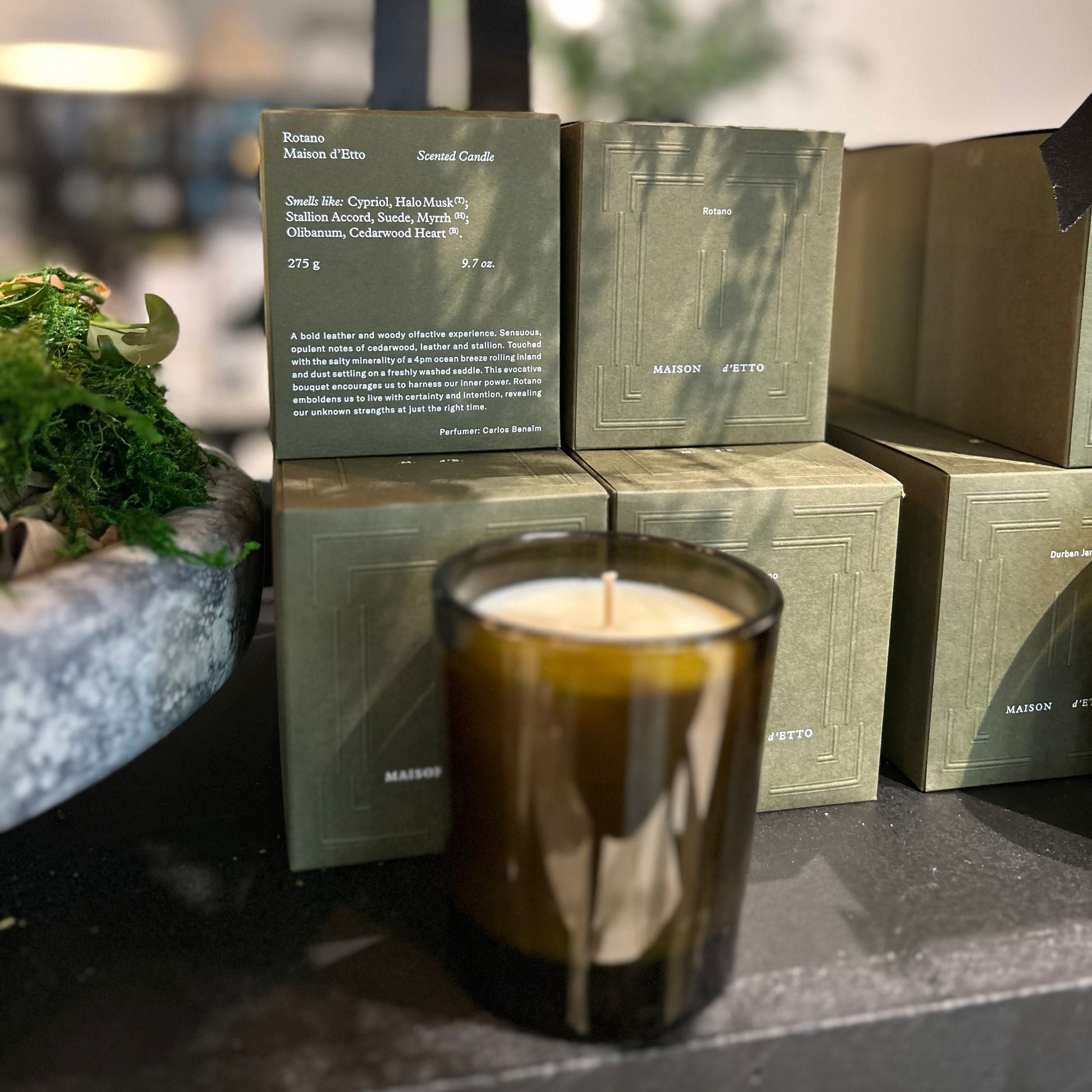 Candle with green packaging on a surface with plants and lights in the background