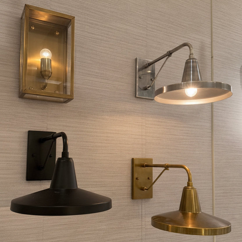 A display of multiple wall sconces mounted on a light gray textured wall, each with its own brass, bronze, and black finish and accompanied by small product information cards.