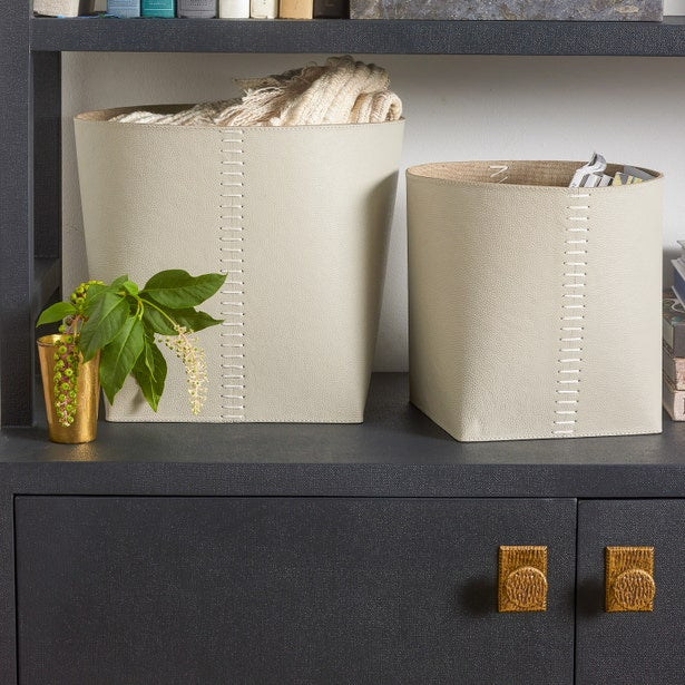 Two beige storage bins on a dark surface with a plant and books in the background.