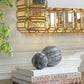 Decorative marble spheres on books with a gold mirror above in a room setting