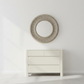 Round mirror with a textured frame above a white dresser against a light gray wall.