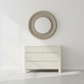 Round mirror with a textured frame above a white dresser against a light gray wall.