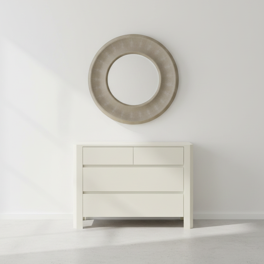 Round mirror with a textured frame above a white dresser against a light gray wall.