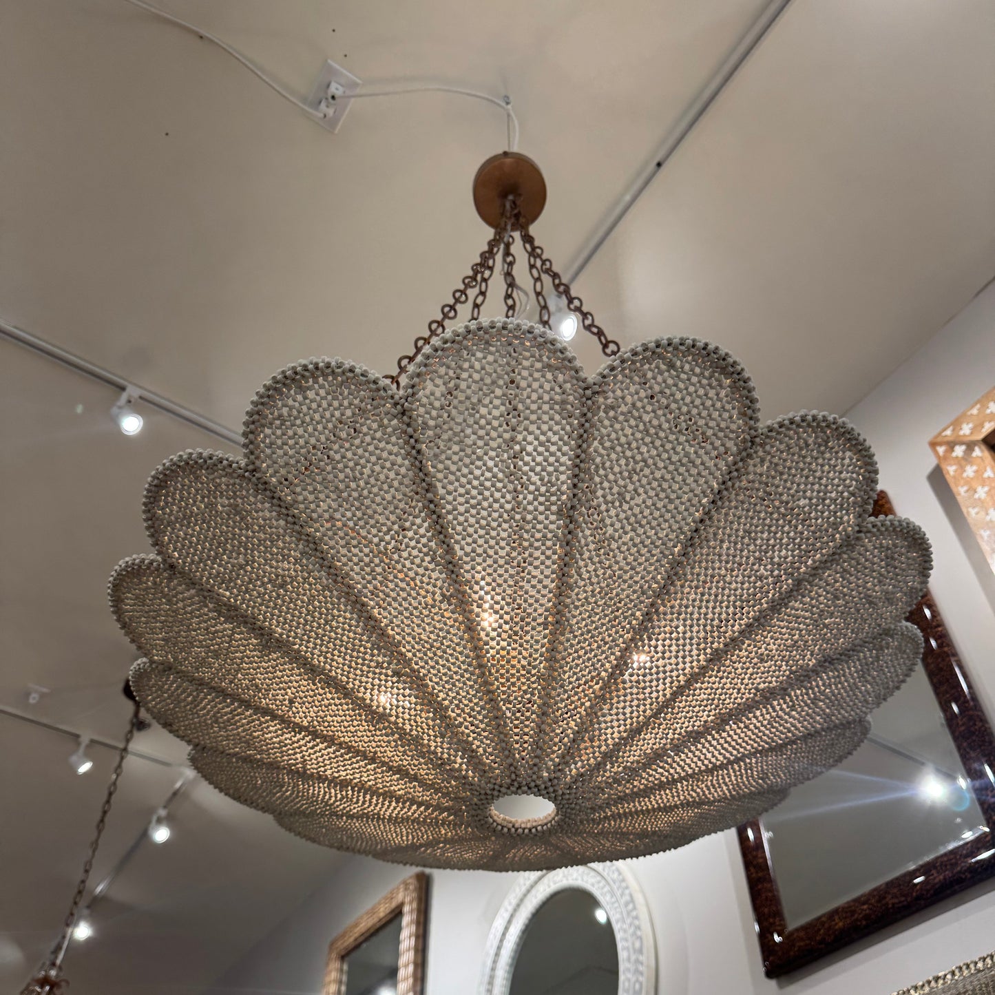 Decorative chandelier hanging from a ceiling with mirrors and lights in the background.