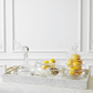 Decorative tray with glass containers holding lemons and other items on a white surface.