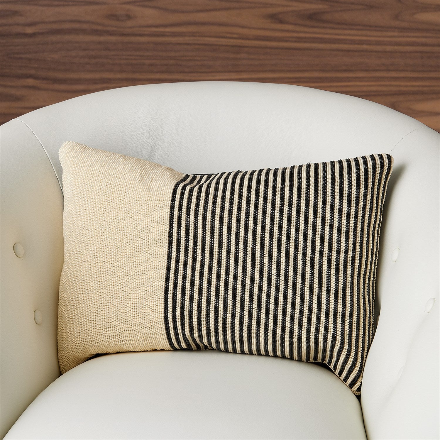 Decorative pillow with beige and black striped pattern on a white armchair.