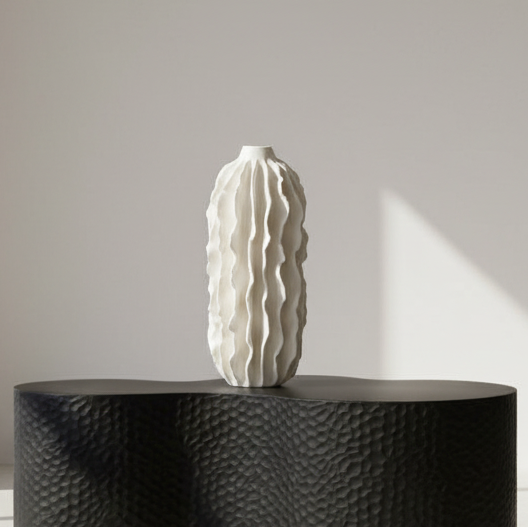 White textured vase on a black textured pedestal against a neutral wall.