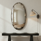 Oval mirror with textured surface on a white wall above a black console table.