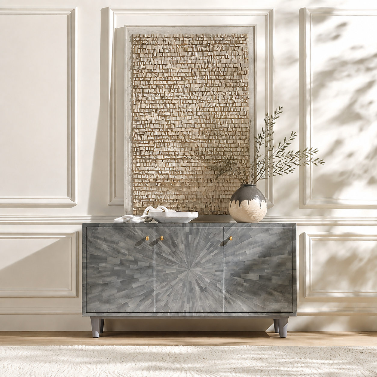 A gray faux horn sideboard with a starburst pattern and small gold knobs, styled in a bright room with a woven wall art piece and a vase behind it.