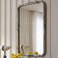 Decorative mirror with a marble-like frame on a wall with striped wallpaper.
