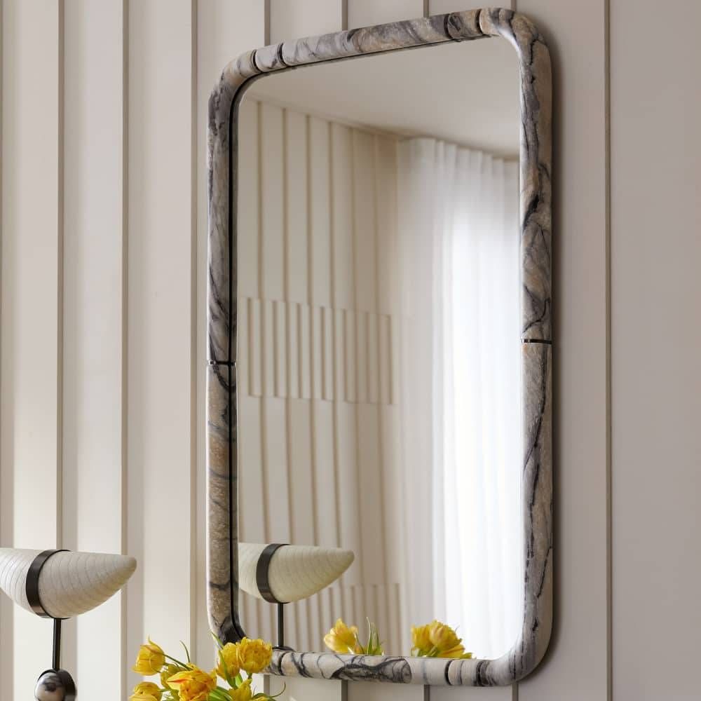 Decorative mirror with a marble-like frame on a wall with striped wallpaper.