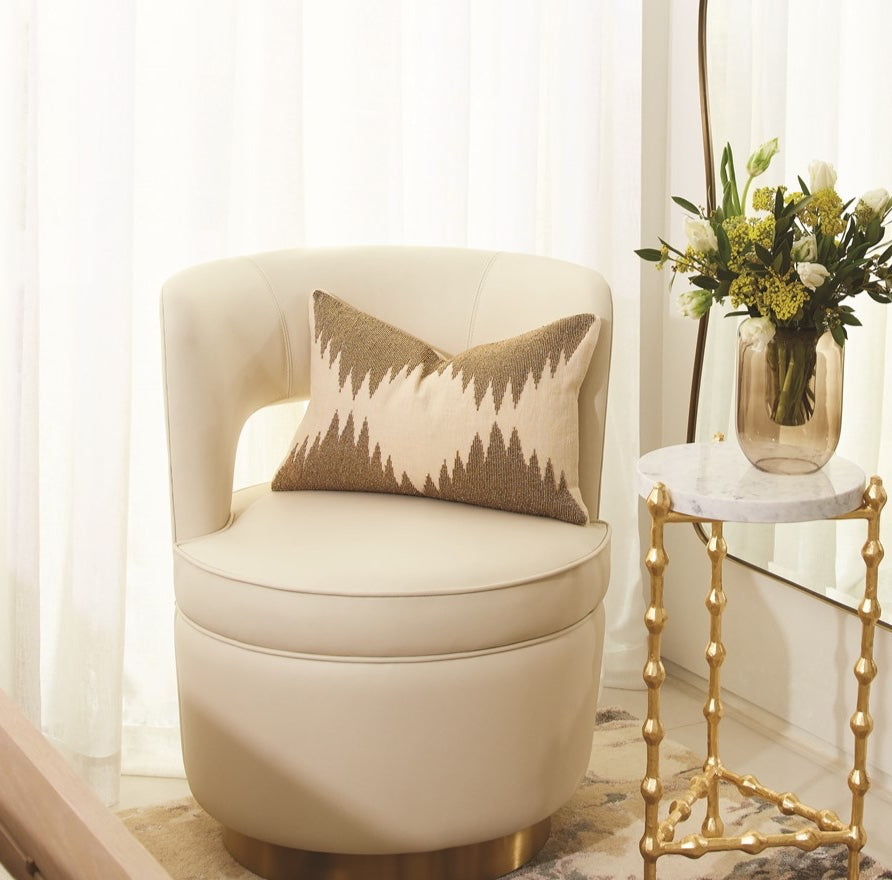 Beige armchair with a decorative pillow next to a gold side table with a vase of flowers.