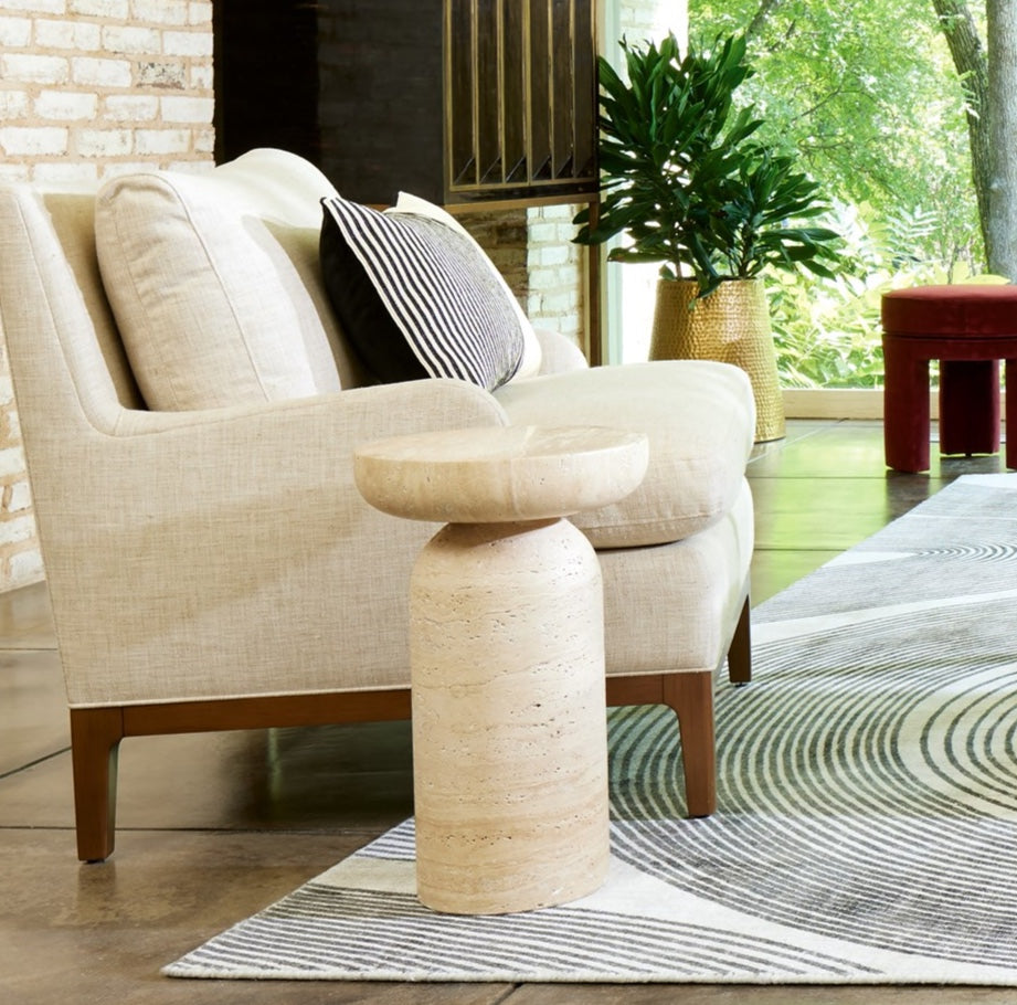 Beige armchair with striped pillow on a rug in a room with a plant and window.