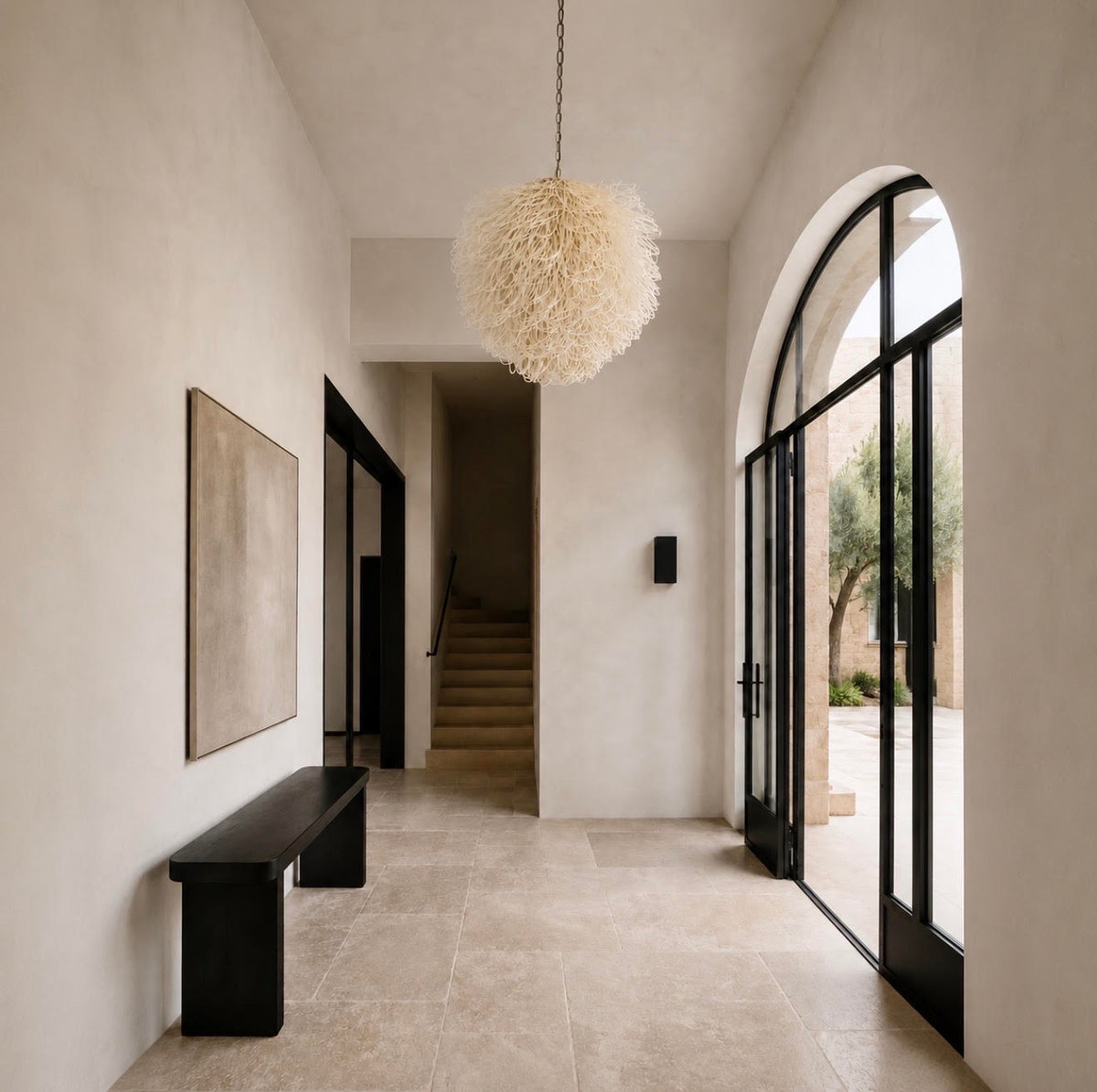 A loosely looped bleached rattan white chandelier hung in a neutral hallway