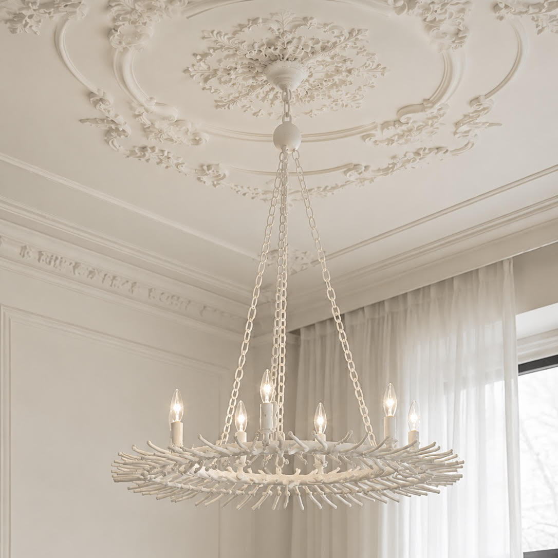 A large, ornate white chandelier with a leaf-like circular frame and multiple candle-style bulbs, hanging from chains in a decorated room with a detailed white ceiling medallion and curtains.