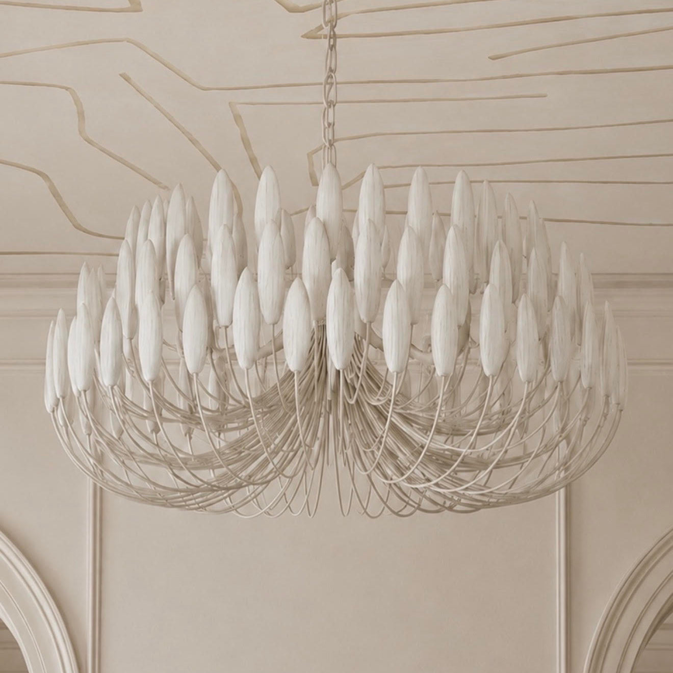 A large white chandelier with multiple elongated teardrop-shaped glass shades and a silver-toned wire frame, hanging from a chain in an elegant cream-colored room with decorative molding on the ceiling and walls.