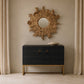 A modern black wood credenza with gold legs and square gold handles, styled in a room setting under a rustic sunburst mirror.