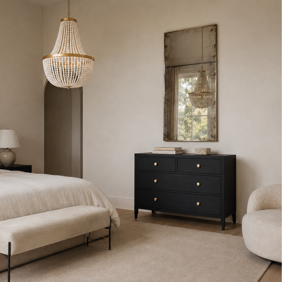 A styled bedroom interior featuring a black wooden dresser with brass knobs, a large woven chandelier, a cream upholstered bed, and a matching bench on a neutral beige carpet.