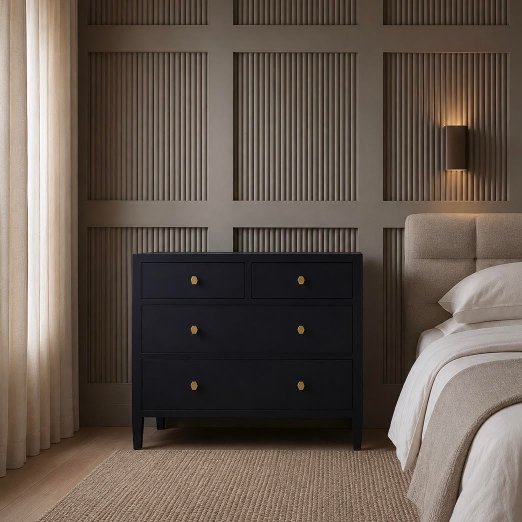 A dark navy blue three-drawer nightstand with small gold knobs stands beside a bed in a modern bedroom with beige walls, textured paneling, and a woven rug.