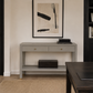 A light gray console table with two drawers and an open lower shelf, styled in a modern living room setting with a framed abstract print above it.