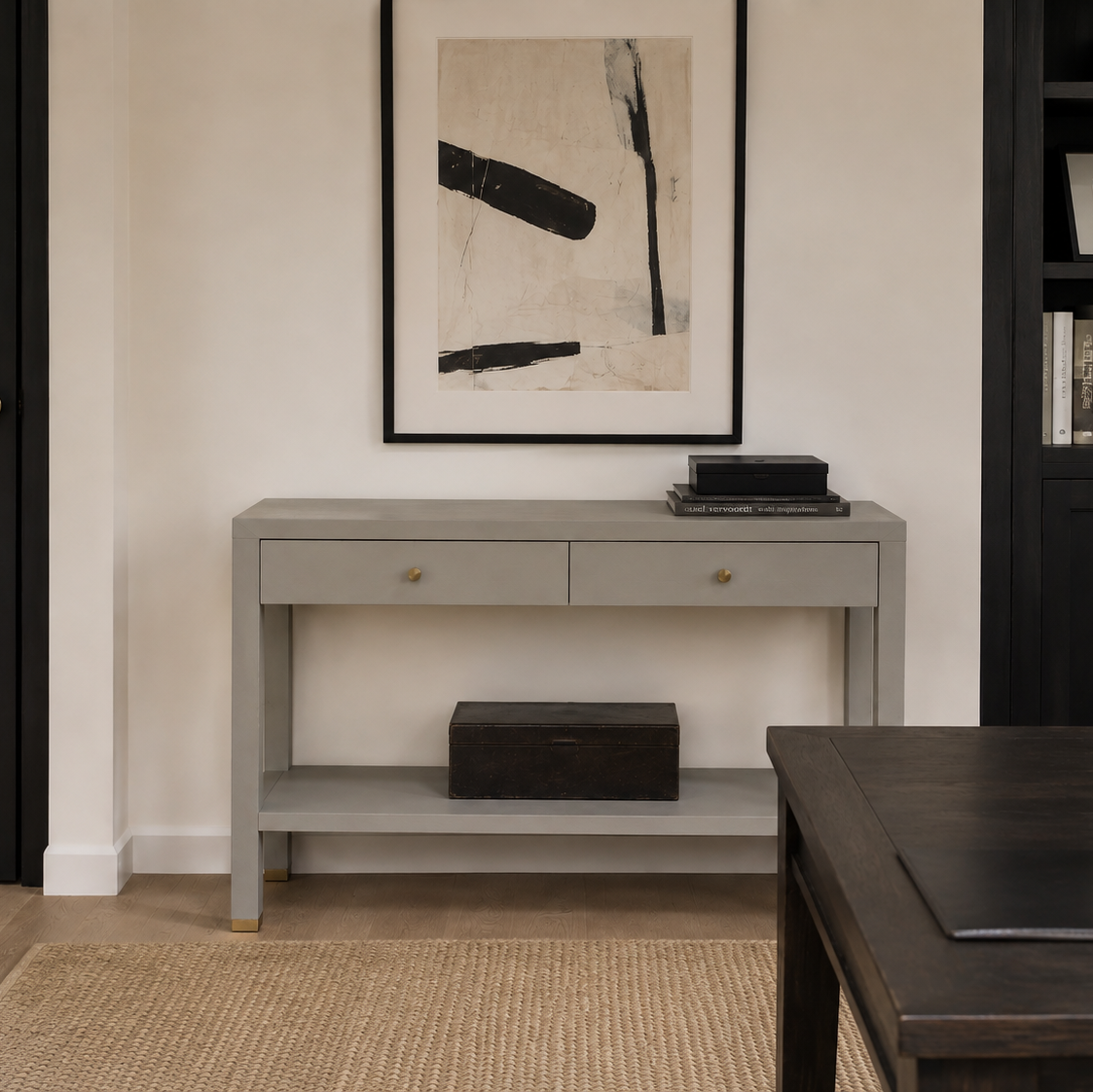 A light gray console table with two drawers and an open lower shelf, styled in a modern living room setting with a framed abstract print above it.