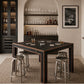 A dark wood and black bar table with six round silver metal bar stools, styled in a modern home bar setting with wine glasses, bottles, and glasses on the table.